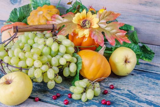 Green grapes in a basket and ripe apples, red cranberries, orange decorative pumpkin and squash with leaves on the wooden background