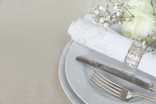 Beautiful decorated table with empty white plates, linen lacy napkin, cutlery and white rose flowers on tablecloths, with space for text