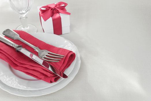 Beautiful decorated table with white plates, gift box with a red ribbon, cutlery and wine glass on tablecloths, with space for text