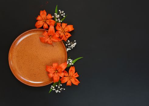 Beautiful orange flowers lilies and clay plate, isolated on a black background