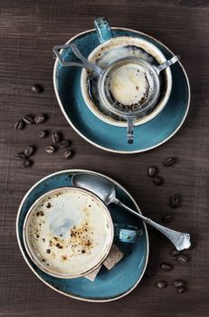 Two cups of coffee, coffee beans, pieces of sugar and teaspoons on a wooden table; top view