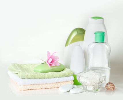 Green and white containers with different cosmetics, soap and a stack of towels, isolated on white background