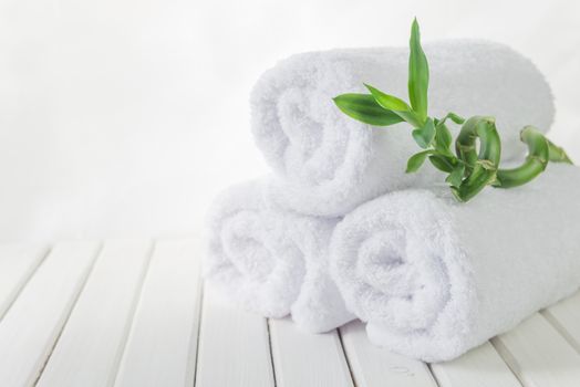 SPA concept: stack of three rolls of white fluffy bath towels with green Lucky bamboo plant on the background of white boards