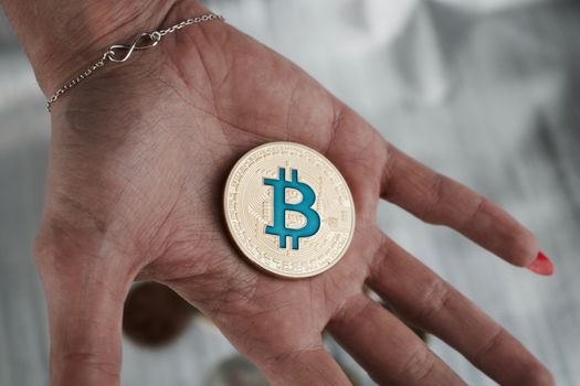 Cryptocurrency physical gold bitcoin coin on hand near infinity sign.