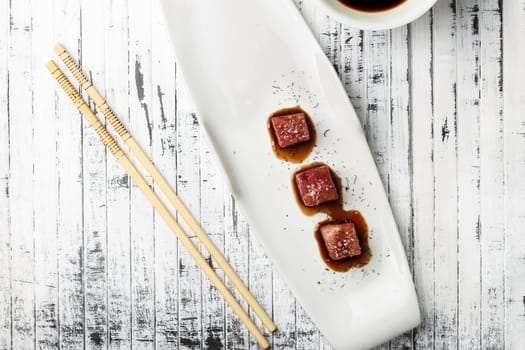 Tuna sashimi dipped in soy sauce,  thick salt and dill on old white wooden board with chopsticks and sauce bowl. Viewed from above. Raw fish in traditional Japanese style. Horizontal image.