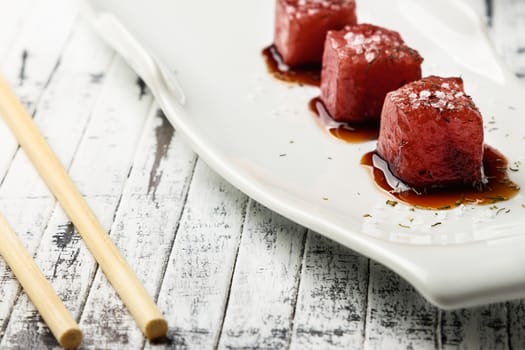 Tuna sashimi dipped in soy sauce,  thick salt and dill on old white wooden board with chopsticks. Raw fish in traditional Japanese style. Horizontal image.