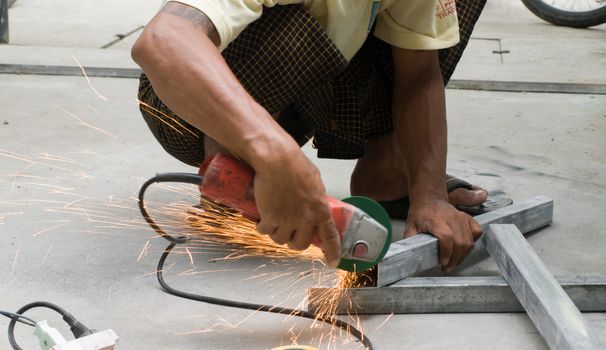 COLOR PHOTO OF WORKER CUTTING STEEL WITH ELECTRIC WHEEL GRINDER