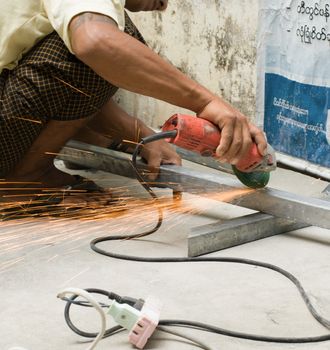 COLOR PHOTO OF WORKER CUTTING STEEL WITH ELECTRIC WHEEL GRINDER
