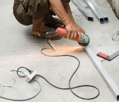 COLOR PHOTO OF WORKER CUTTING STEEL WITH ELECTRIC WHEEL GRINDER