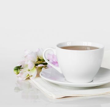 Hot tea in a white porcelain cup with saucer,linen napkin and flower in the backdrop, on a white background, with space for text