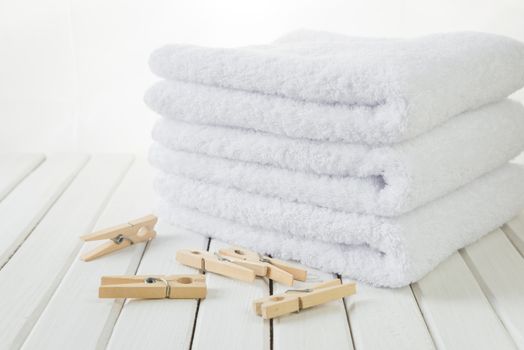Stack of three white fluffy cotton bath towels and wooden clothespins on the background of white boards