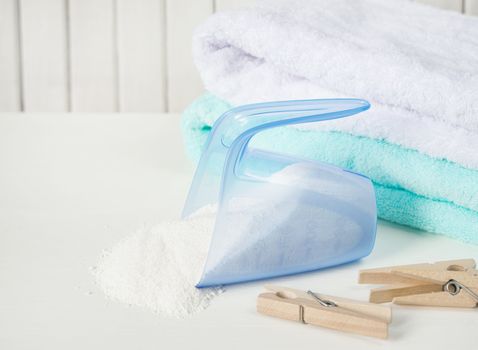 Stack of white and blue fluffy bath towels, washing powder in measuring cup and wooden clothespins on the background of white boards