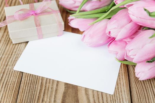 Tulips flowers, empty greeting card and gift box with a bow on a background of old wooden boards