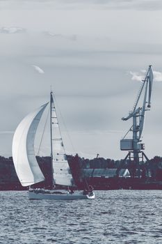 Sailboat moving past the cargo crane in evening, Latvia