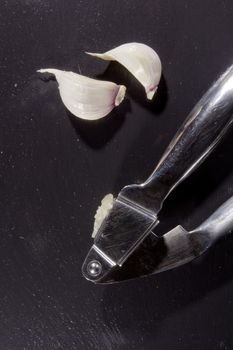 Garlic press and cloves of garlic, lying on a background of a stone board