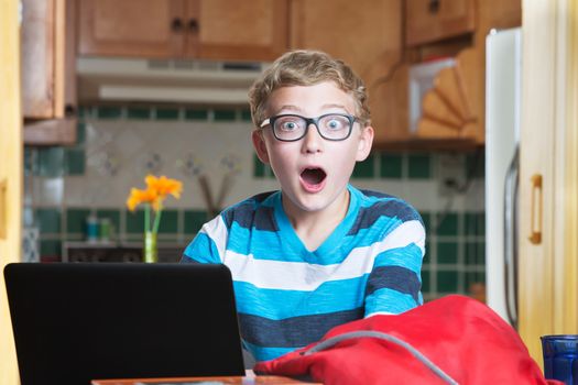 Cute teen boy in eyeglasses with laptop and surprised expression
