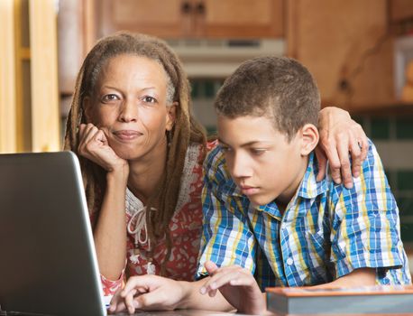 African-American mother supervises her teenaged son as he studies on his computer