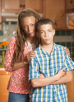 African-American mother holds her irritated teenaged son while standing in kitchen