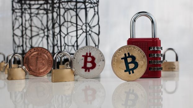 Digital currency physical brass, silver and gold bitcoin coins near padlocks.