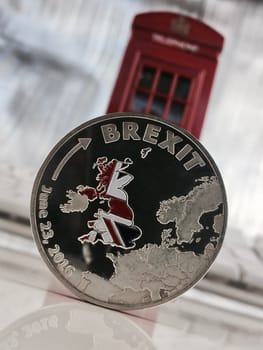 Physical silver brexit coin near red telephone box. Europe leaving.