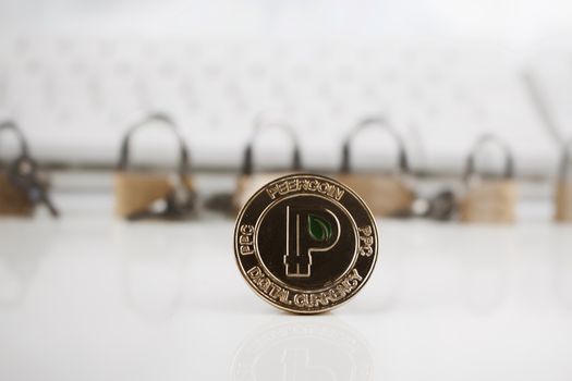 Cryptocurrency physical gold peercoin coin near gold padlocks and keyboard.