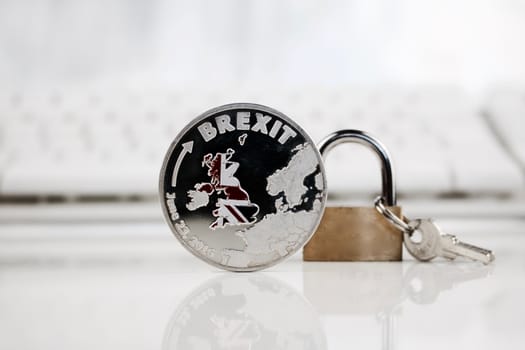 Physical silver brexit coin near gold padlock.