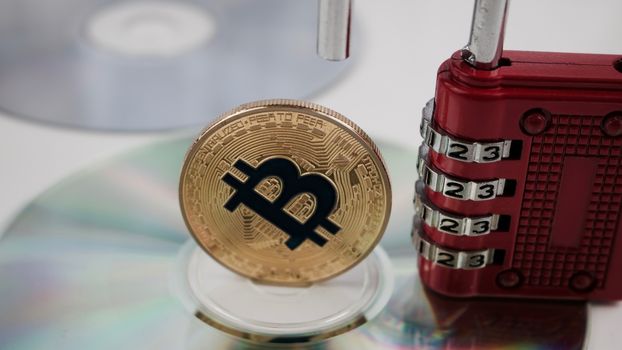Cryptocurrency physical gold bitcoin coin on the CD near red numeric padlock.