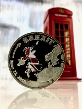 Physical silver brexit coin near red telephone box.