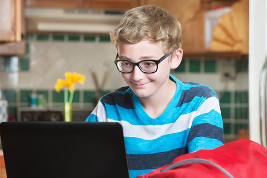 Grinning single boy in eyeglasses and striped shirt using laptop