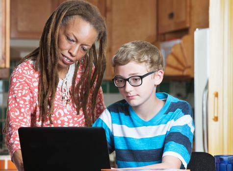 Foster parent helping child in eyeglasses working on laptop