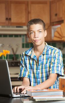 Grinning African-American male student in kitchen with books and open laptop computer