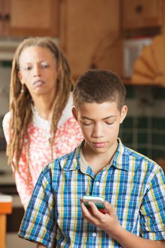 Concerned mother attempts to spy over shoulder of her teenaged son as her reads message on his mobile phone