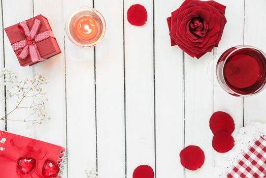 Concept of Valentine's Days holiday: festive table with glass of wine, red rose, gift box with bow and burning candle; top view, with copy-space