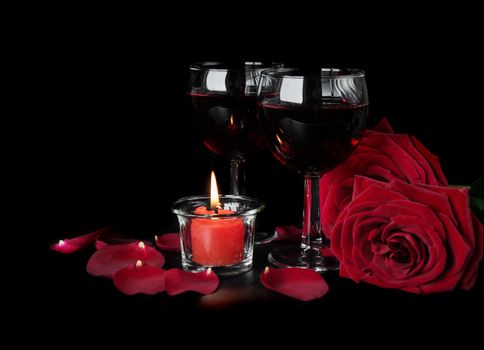 Valentine's Days concept: two glasses of red wine, two red roses and a burning red candle isolated on a black background