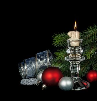 Christmas card with red and silver Christmas balls, burning candle, decorative ribbon and branches of spruce, isolated on a black background