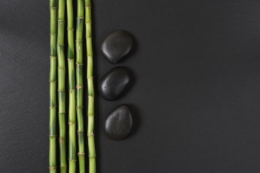 Spa concept with black basalt massage stones and a few stems of Lucky bamboo on a black background; with space for text