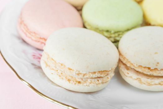 Several multicolored macaroons pastel colors on the porcelain plate on pink background