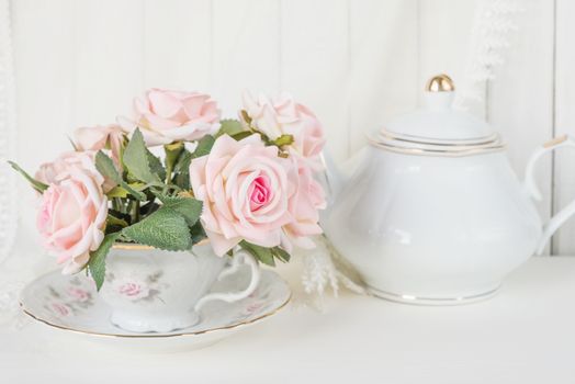 Beautiful still life: a graceful porcelain cup, white china teapot and pink rose flowers