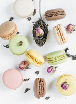 Multicoloured macaroons, tea, dried rose buds and teaspoon on white background; top view, flat lay