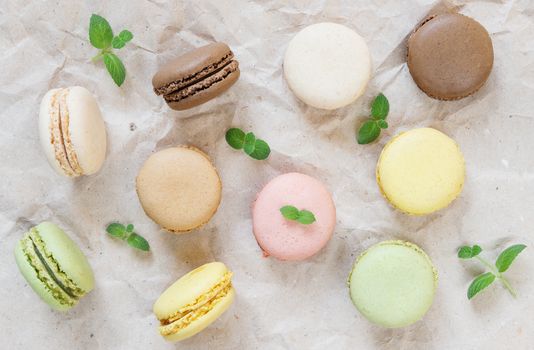 Multicoloured macaroons and green mint leaves on the background of wrapping paper; top view, flat lay