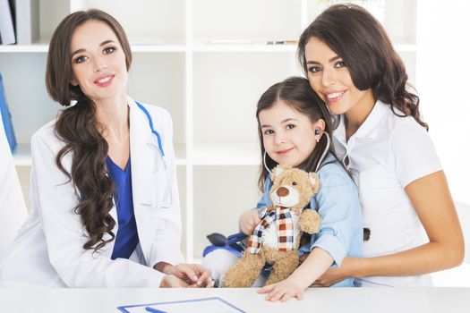 Happy mother and child with teddy bear and stethoscope at pediatrician office