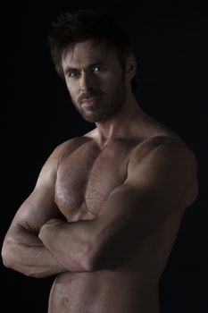 Dark shot of healthy muscular naked young man with crossed hands