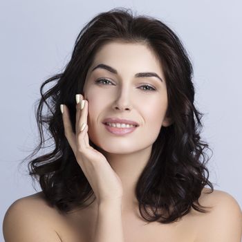 Portrait of a beautiful woman with perfect skin and dark curly hair touching face, skincare concept