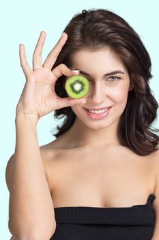 Young smiling woman looking through slice of kiwi