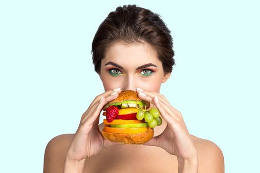 Young woman eating hamburger made of fruits and vegetables, healthy eating concept