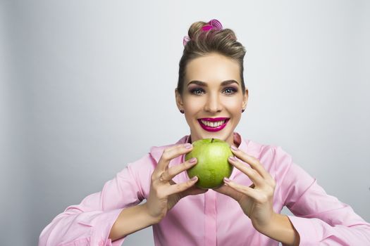 Funny smiling blond woman with bright pink make-up holding green apple