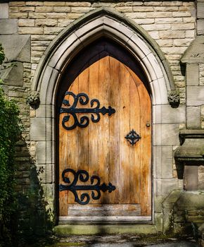 Arched stone entrance to medieval style building. Worn wooden door with ornate back hinges. Gives sense of mystery and exploration.
