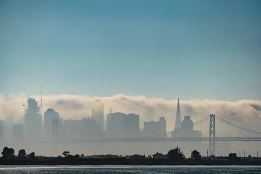 Fog rolling over san Francisco bay area. Silhouette of city skyline can be seen through it. Blue skies above.