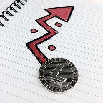 Digital currency physical silver Litecoin coin and red arrow in notebook.