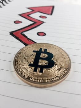 Cryptocurrency physical gold bitcoin coin and red arrow in notebook.